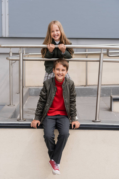 happy preteen kids in stylish bomber jackets posing near metallic handrails near mall  - Photo, Image