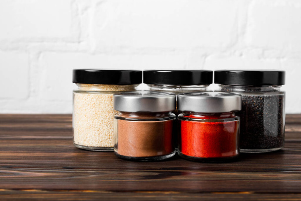 Bright fragrant spices in glass jars of different sizes on a wooden table. Proper storage of spices. - Valokuva, kuva
