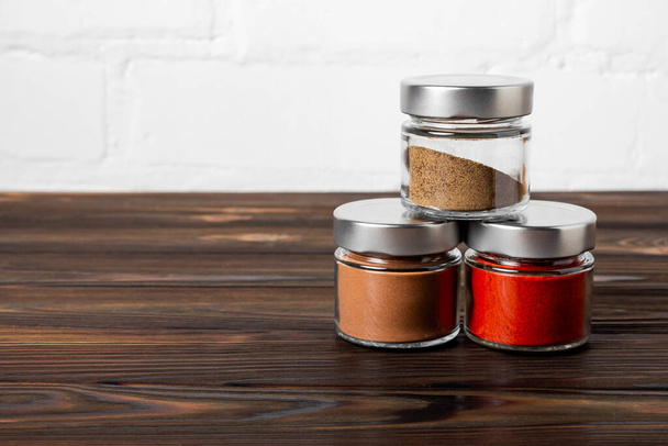 Bright fragrant spices in glass jars of different sizes on a wooden table. Proper storage of spices. - Valokuva, kuva