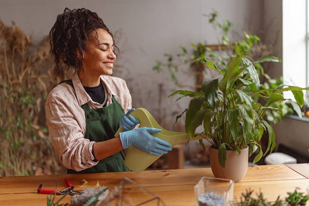 Χαμογελαστή γυναίκα ανθοπώλης που φροντίζει το φυτό ποτίζοντάς το σε ανθοπωλείο. Υψηλής ποιότητας φωτογραφία - Φωτογραφία, εικόνα