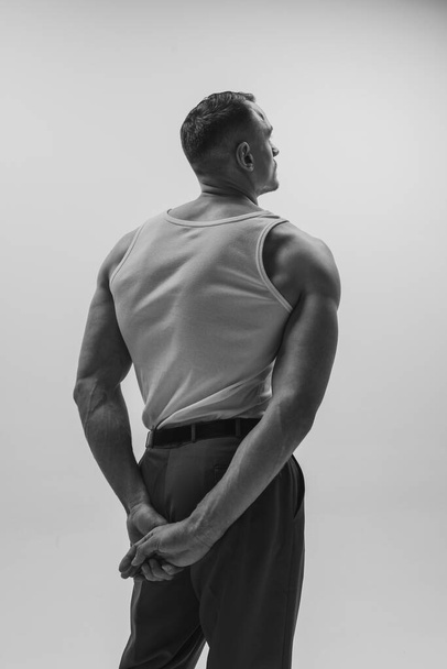 Black and white portrait of muscular man with wide back posing over grey studio background. Masculinity and confidence. Concept of mens health, beauty, fashion, ad. Back view. Monochrome - Fotó, kép