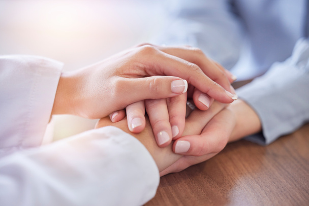 Holding hands, doctor and patient at desk for comfort, talking and communication for bad news, mental health or support. Therapist woman, cancer and together for empathy, care or wellness in hospital. - Photo, Image