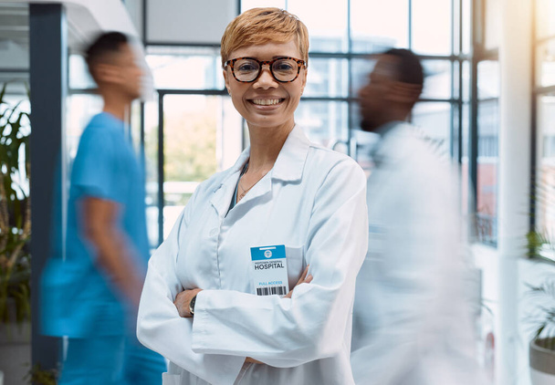 Πορτρέτο, γιατρός και μαύρη γυναίκα σε ένα πολυάσχολο νοσοκομείο αγκαλιά σταυρωμένα με θολή κίνηση. Υγειονομική περίθαλψη, ηγεσία και εμπιστοσύνη σε επαγγελματία ιατρό σε κλινική για υγειονομική περίθαλψη. - Φωτογραφία, εικόνα