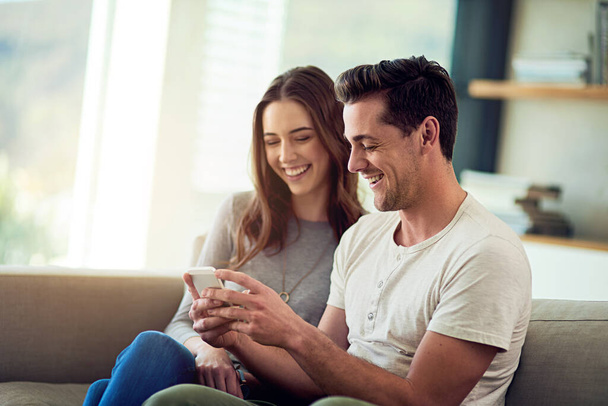 Prise de vue d'un jeune couple heureux utilisant un téléphone ensemble sur le canapé à la maison. - Photo, image