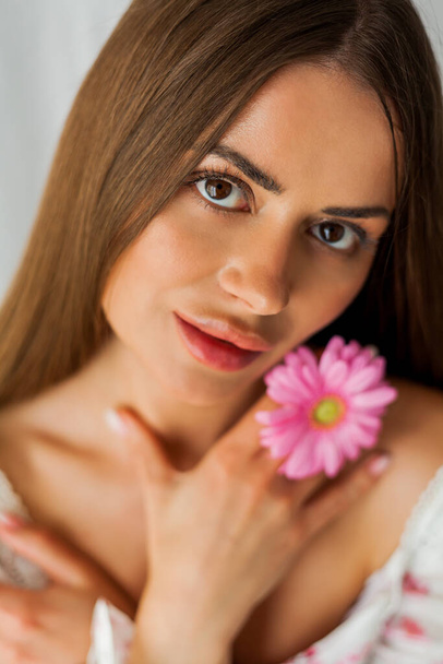 Portrait of young beautiful long-haired brown-eyed woman with pink gerbera on white background. Spring. Holidays. - Φωτογραφία, εικόνα