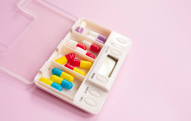 Plastic box with different pills on light pink background. Space for text - Foto, imagen