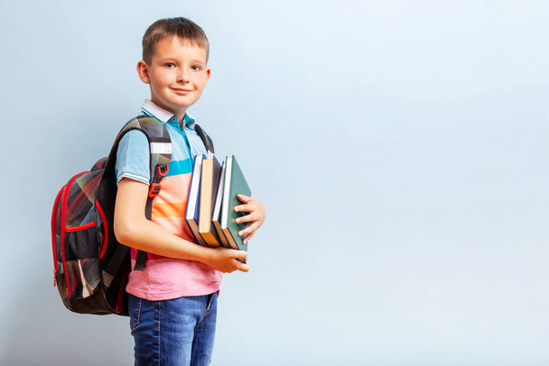 Netter Schuljunge mit Rucksack mit Büchern auf blauem Hintergrund für Bildungskonzept. - Foto, Bild