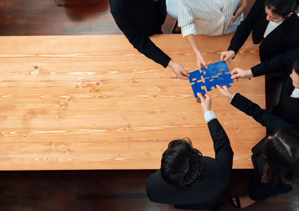 Top view businesspeople and colleagues in formal wear putting jigsaw puzzles together over meeting table with financial report papers in harmony office for team building concept. - Foto, Imagen