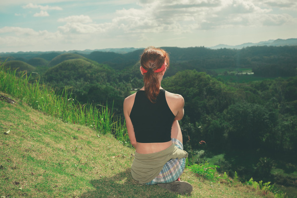 Jonge vrouw zitten op een heuvel en het bewonderen van de weergave - Foto, afbeelding