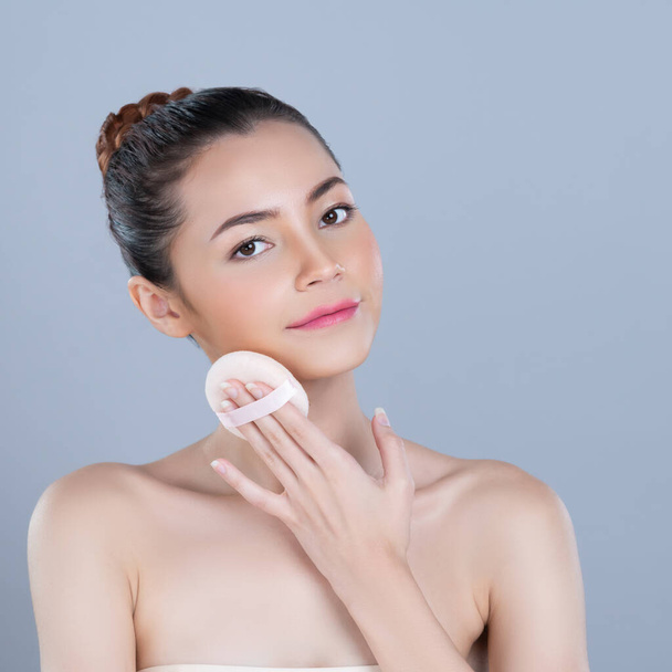 Glamorous beautiful female model applying cushion powder for facial makeup concept. Portrait of flawless perfect cosmetic skin woman put powder puff on her face in isolated background. - Photo, Image