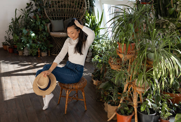 Attractive Asian girl sitting in chair relaxing in garden with many indoor green plants. Green Home.  - Fotoğraf, Görsel