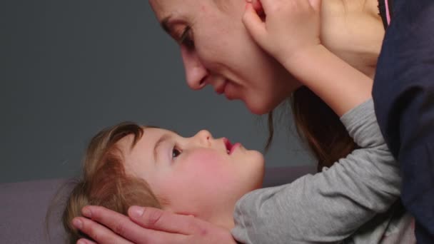 Close up shot of young mother is playing and kiss with her little girl in in a morning on gray background. Concept of children, baby, parenthood, childhood, life, maternity, motherhood. - Metraje, vídeo
