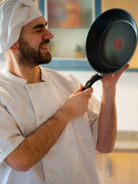 portré egy fiatal szakállas szakács mosolyog, miközben egy rozsdamentes serpenyő - Fotó, kép