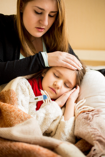 молодая обеспокоенная мать проверяет температуру больных дочерей
 - Фото, изображение