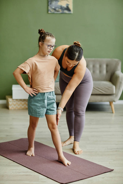 Vertical full length portrait of young girl with down syndrome exercising indoors with female instructor assisting - Фото, зображення