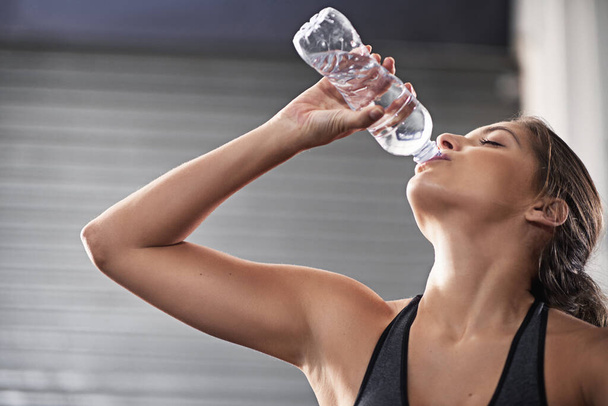 Manteniendo su cuerpo hidratado. una joven bebiendo de su botella de agua en el gimnasio - Foto, Imagen
