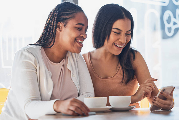 Women friends, coffee shop and phone with smile, happy and laugh at comic meme on social network. Gen z black woman, smartphone and relax in cafe with blog, funny video or texting app ux on internet. - Fotoğraf, Görsel