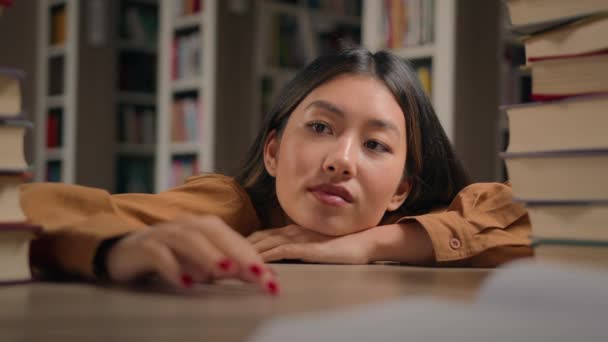 Unavený zamyšlený mladý asijské žena ležící na stole s knihami příprava na vyšetření v univerzitní knihovně nudit přemýšlivý líný student dívka dívá pryč myšlení snění pocit únavy po studiu - Záběry, video
