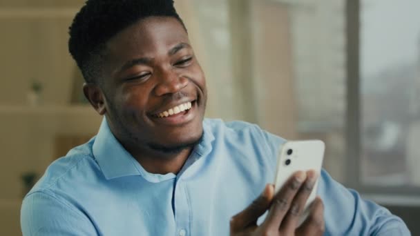 Appel vidéo d'affaires souriant homme d'affaires afro-américain parlant téléphone mobile connexion virtuelle utiliser l'application de conférence en ligne sur smartphone. Millénaire homme ethnique entrepreneur employé de bureau bavarder en intérieur - Séquence, vidéo