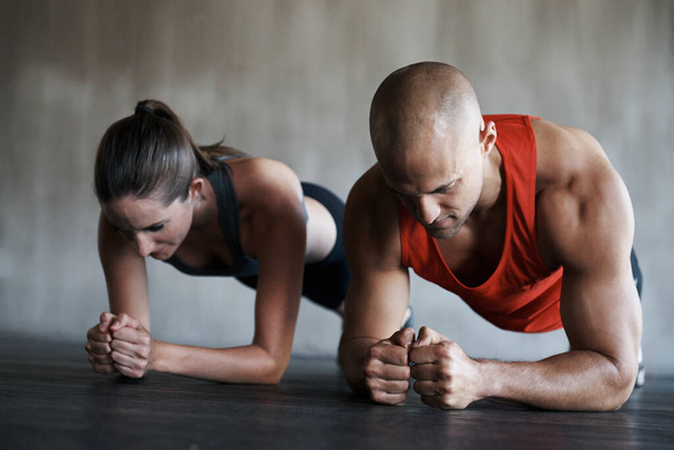 Tiro de un hombre y una mujer haciendo ejercicios de tablón en el gimnasio. - Foto, imagen