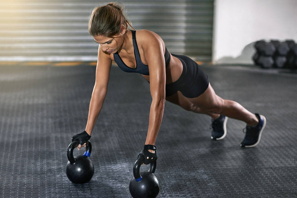 She trains like a beast. Full length shot of a young woman working out with kettle bells at the gym - Foto, immagini