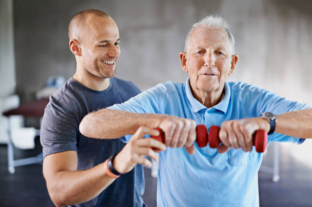 Tiro de um fisioterapeuta ajudando um homem idoso com pesos. - Foto, Imagem