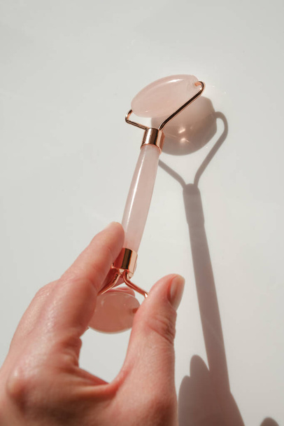 gua sha roller in a hand on a light background.beauty devices.Gua sha facial massage device.Roller massager made of pink natural stone - 写真・画像