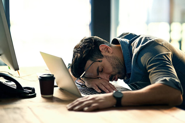 仕事の遅い夜の間に彼の机の上で眠っている疲れ若いビジネスマンのショット. - 写真・画像