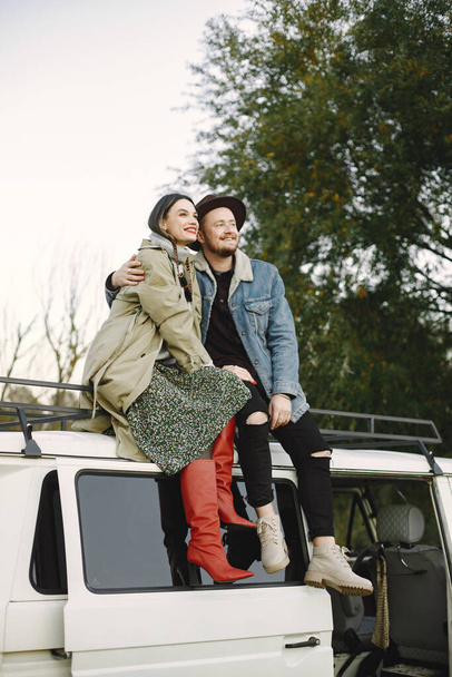Man and woman in fashion clothes sitting on top of the bus. Man wearing jacket and a black hat and woman coat and red boots. Photo of romantic couple on the top of retro bus. - Photo, image