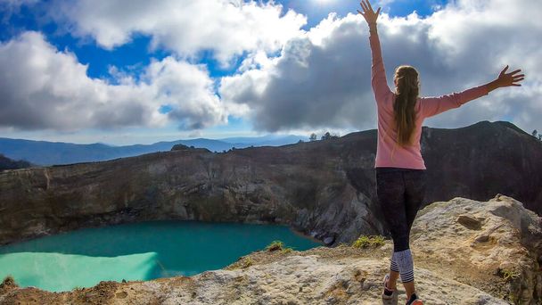 Woman standing at the volcano rim with arms spread and watching the Kelimutu volcanic crater lakes in Moni, Flores, Indonesia. Woman engages with life and has the feeling of freedom - Foto, Imagen