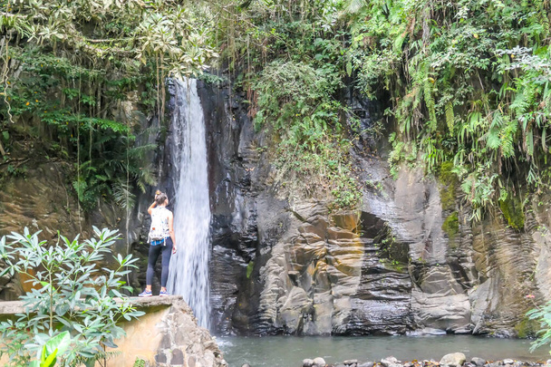 A girl is admiring the Murukeba waterfall in the small town of Moni, Island of Flores, Indonesia. The surrounding rainforest creates a magical atmosphere of inspiration and dedication. - Foto, imagen