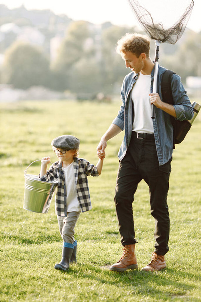 Dad and his child boy spend time outdoors together. Curly toddler boy wearing a plaid shirt and a hat. Boy holding a hand of his father. - Fotó, kép