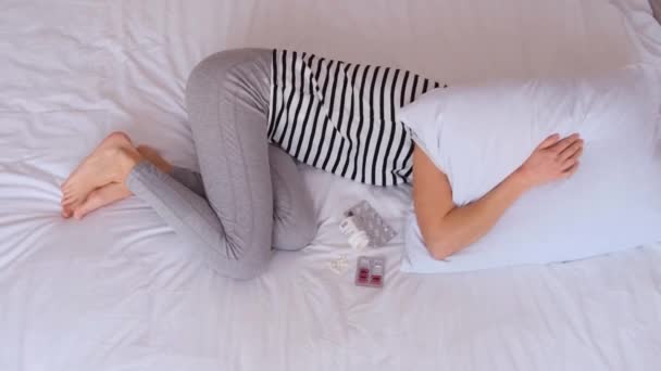 Eine kranke Frau liegt auf einem weißen Bett und bedeckt ihren Kopf mit einem weißen Kissen. Leiden unter Schmerzen. Sie hat ein Problem. Isolation mit Lebensfreude - Filmmaterial, Video