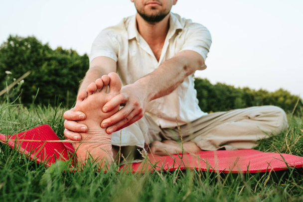 a young man is doing yoga on a red carpet in nature, holding hands by the leg - Fotoğraf, Görsel