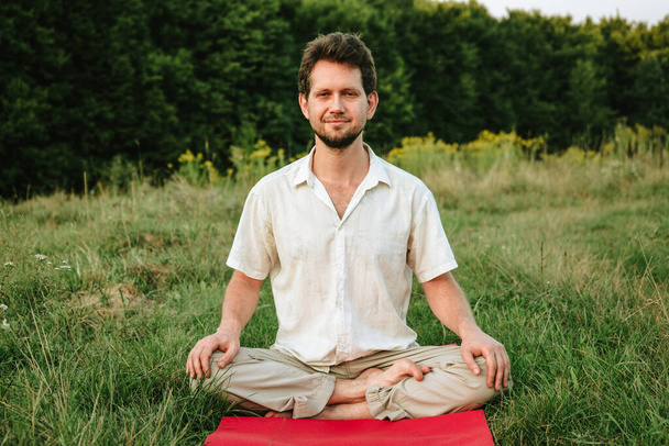 a young man doing yoga in nature with a smile, sitting in the lotus position - Photo, Image