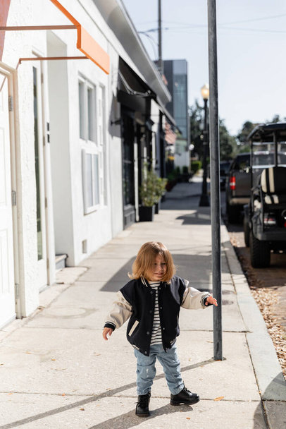 マイアミの路上を歩くスタイリッシュな爆撃機ジャケットの幸せな赤ちゃんの女の子の完全な長さ  - 写真・画像
