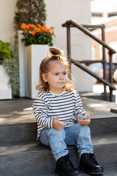 taapero tyttö pitkähihainen paita ja farkut istuu portaissa talon lähellä  - Valokuva, kuva