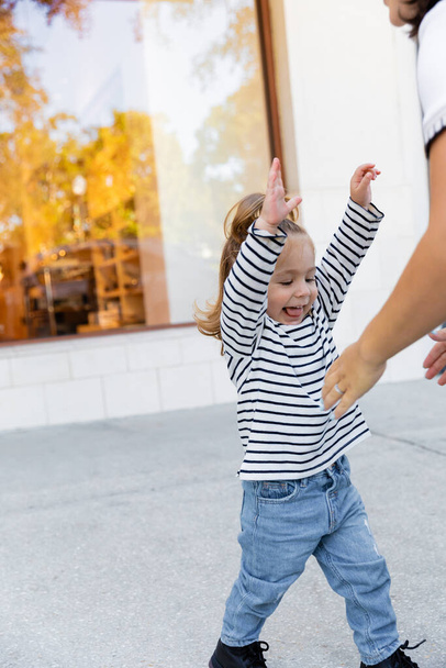happy toddler girl standing with outstretched hands near mother on street in Miami  - Фото, зображення