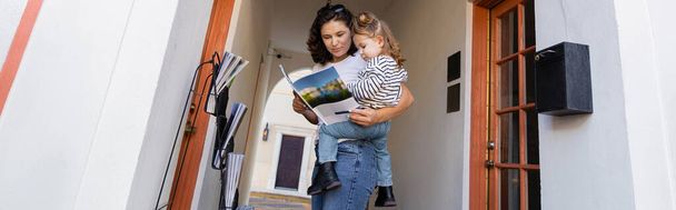 Мати читає журнал і тримає маленьку дочку біля будинку в Маямі, банер.  - Фото, зображення