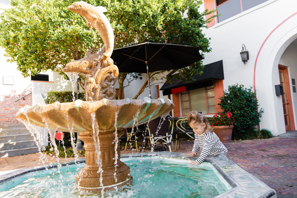 toddler girl in striped long sleeve shirt wetting hands in fountain water in Miami  - Foto, immagini