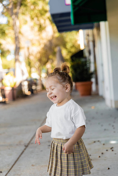 gelukkig peuter meisje in rok en t-shirt glimlachen met gesloten ogen buiten  - Foto, afbeelding