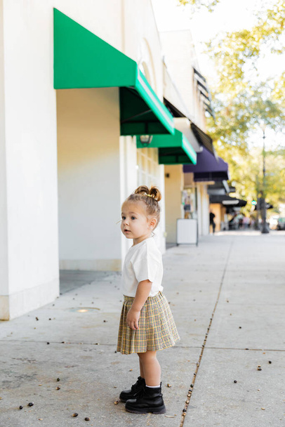full length of toddler child in skirt and white t-shirt standing near acorns on ground in Miami  - Foto, Bild