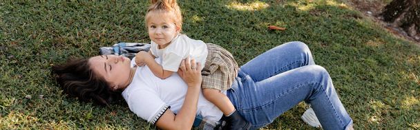 brünette Mutter schmollende Lippen und Liegen im Gras mit Kleinkind Baby Mädchen, Banner  - Foto, Bild