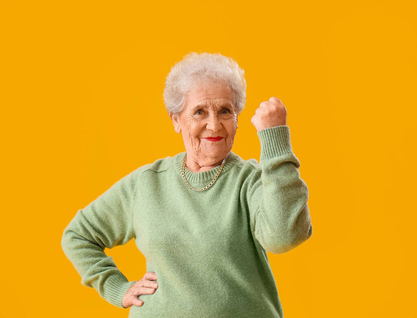 Boldog idős nő zöld pulóver sárga háttér - Fotó, kép