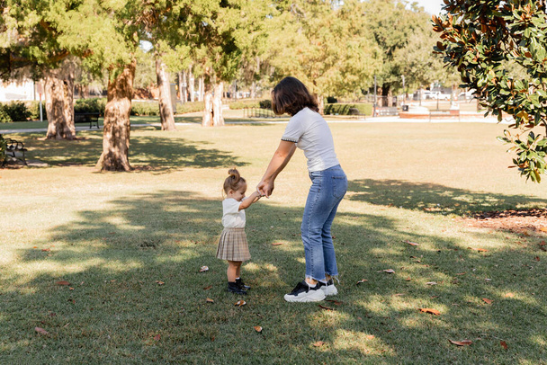 full length of mother in jeans holding hands with toddler daughter in park of Miami  - 写真・画像