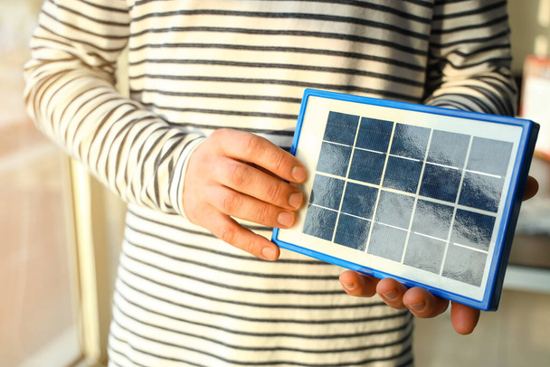 Young man with portable solar panel at home, closeup - Foto, Imagem
