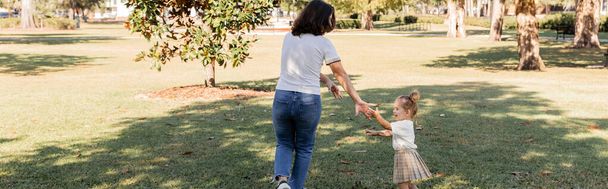 Брюнетка мать в джинсах играть с счастливой дочкой малыша в парке Майами, баннер  - Фото, изображение