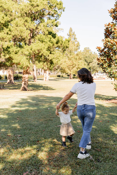 brunette mother holding hands with happy toddler daughter while playing in park of Miami  - Fotoğraf, Görsel