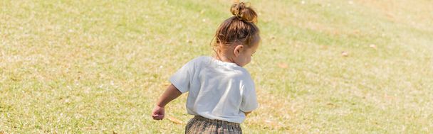 πίσω όψη του κοριτσιού νήπιο σε λευκό t-shirt με τα πόδια σε πράσινο γρασίδι, πανό  - Φωτογραφία, εικόνα