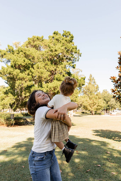 Miami Parkı 'nda birlikte oynarken küçük kızını kaldıran neşeli bir anne.  - Fotoğraf, Görsel